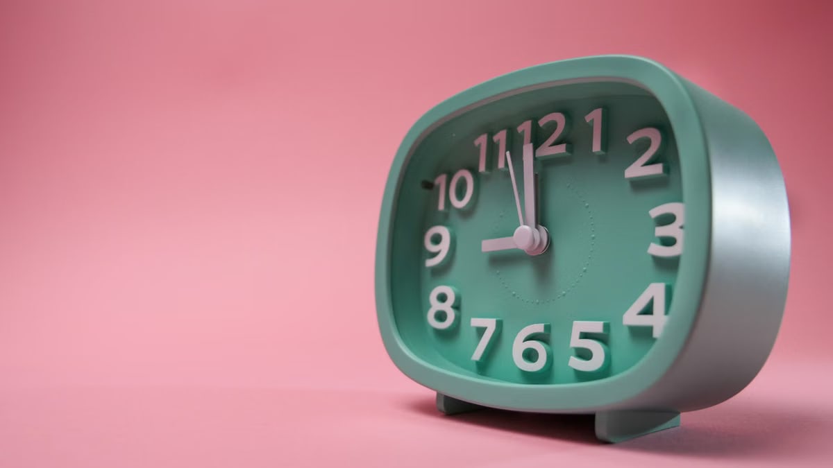 A green analog clock sits against a pastel pink background, showcasing a vibrant contrast.